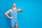 Portrait of joyful pensioner showing thumb up approve sign wearing striped swimwear isolated over blue background