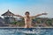 Portrait of joyful slender man with chest hair, emerges from pool, water splashes, shows tongue and hands up, on hotel roof.