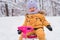 Portrait of a joyful toddler 12-23 months old sitting on a children`s snowcat in a winter park. Active lifestyle in winter