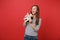 Portrait of joyful young woman in striped clothes holding and playing with teddy bear plush toy isolated on bright red