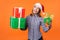 Portrait of joyous beautiful brunette woman in santa hat and checkered shirt standing, holding gift boxes and looking at camera