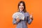 Portrait of joyous brunette woman wearing checkered shirt holding money. indoor studio shot isolated on orange background