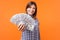 Portrait of joyous cute brunette woman wearing checkered shirt holding money. indoor studio shot isolated on orange background