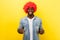 Portrait of joyous funny carefree man in red curly wig, showing thumbs up. indoor studio shot isolated on yellow background