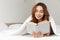 Portrait of joyous woman lying in bed under white blanket in bed