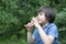 Portrait of kid drinking orange juice and looking out in hot sunny day, Thirsty boy drinking soda sitting  in the park, happy