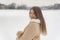 Portrait of laughing girl in beige sheepskin coat standing half turn on snowy terrain background