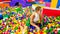 Portrait of laughing young woman falling in pool with lots of colorful plastic balls on the children palyground at