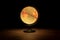 A portrait of a light emitting globe stand on a wooden floor in a dark room. It depicts earth and is perfect for exploring the
