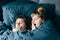 Portrait of light hair long hair mother and daughter on pillow under the duvet together yawn in soft sleepy morning light on blue