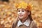 Portrait liitle cute girl with crown of leaves in autumn park