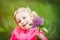 Portrait of little 3 years old blonde girl in pink jacket with branch of purple lilac in hand. Defocused lilac and smiling kids