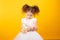 Portrait of a little adorable curly girl, looking frowned on a alarm clock, over yellow background. copy space.