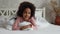 Portrait little African American girl lying under covers, looking at camera and smiling. Teenage girl in pajamas lies on