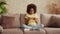 Portrait little African American girl in plays a game on smartphone. Teenage girl sits on gray sofa in hall against