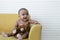 Portrait of Little African newborn baby girl wear diaper smiling and holding brown bear doll while sitting on yellow sofa at home