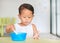 Portrait of little Asian baby boy eating cereal with cornflakes and milk stains around mouth on the table. Children having