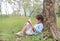 Portrait little Asian child girl reading book in park outdoor sitting lean against tree trunk in the garden outdoor