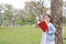 Portrait little Asian child girl reading book in park outdoor standing lean against tree trunk with looking camera