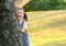 Portrait of little Asian girl play peekaboo by hiding back of tree and smile in park or garden