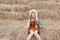 Portrait of little Asian kid girl in a hood on head and warm clothes sitting on pile of straw on a winter season