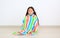 Portrait of little asian kid girl sitting wrapped covered in soft multicolor blanket in room and looking camera