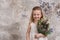 Portrait of a little attractive girl in a white dress with a bouquet in her hands against the background of a grunge wall