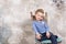 Portrait of a little attractive smiling girl in a blue sweater and pants with her hair folded in her hair sitting on a chair