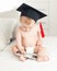 Portrait of little baby boy in diapers wearing graduation cap using on bed and using digital tablet