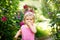 Portrait of little baby girl eating strawberry in garden. Cute child between blossoming roses. Happy healthy toddler