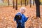 Portrait of a little blond boy with a large DSLR camera on a tripod. Photo session in the autumn park