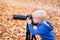 Portrait of a little blond boy with a large DSLR camera on a tripod. Photo session in the autumn park