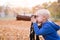 Portrait of a little blond boy with a large DSLR camera on a tripod. Photo session in the autumn park