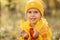 Portrait of little blue-eyed girl in yellow hat with autumn leaves in the park