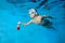 Portrait of a little boy in a Santa Claus hat floating underwater in a pool with a new year`s gift in his outstretched