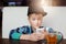 A portrait of little boy wearing modern shirt and cap siting at cafe with a cup of tea holding smartphone looking with great surpr