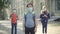 Portrait of little brunette boy in face mask standing in sunlight at school yard with blurred classmates at the