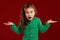 Portrait of a little brunette girl with a long, curly hair posing against a red background.