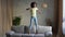 Portrait little cheerful African American girl dancing and jumping on the couch. Teenage girl posing on gray sofa in