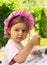 Portrait of little cute girl in a purpule cap eats with appetite a breakfast from a plate with the drawn flower in outdoor cafe