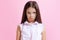 Portrait of little cute offended girl, kid in blouse isolated on pink background. Concept of children emotions, fashion