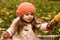 Portrait Of Little Cute Preschool Minor Girl In Orange Beret On Yellow Fallen Leaves Takes Apple From Someone Looks Away