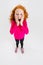 Portrait of little cute redheaded preschool girl in pink sweater posing isolated over white studio background.