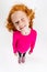 Portrait of little cute redheaded preschool girl in pink sweater posing isolated over white studio background. Winking