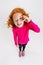 Portrait of little cute redheaded preschool girl in pink sweater posing with one eye closed isolated over white studio