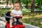 Portrait of a little driver: happy infant child with surprised face sitting barefoot on a red push car outdoor in the park