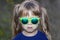 Portrait of little fashionable girl in green sunglasses outdoors