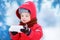 Portrait of little funny boy in red winter clothes having fun with piece of ice