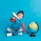 Portrait of little funny school boy with toy paper plane. Showing place on the globe, map. Concept travel, education