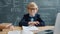 Portrait of little genius in classroom sitting at desk wearing glasses smiling